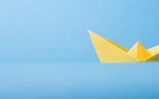 Image of yellow origami boat against a sky blue background