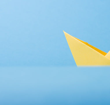 Image of yellow origami boat against a sky blue background